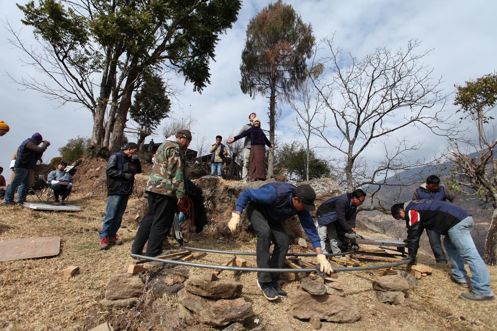 Film crew setting up dolly tracks and equipment on a rugged Bhutanese mountainside